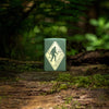 Lifestyle image of Sasquatch Crossing Windproof Lighter standing in the woods on a log