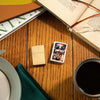 Lifestyle image of Tiger Design Mercury Glass Windproof Lighter laying with a Flag Lighter with books and a cup of coffee