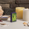Lifestyle image of Cannabis Design Texture Print Leaf Purple Matte Windproof Lighter standing on a side stand with candles and burning incents in the background.